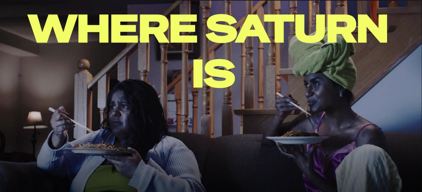 Where Saturn Is key art: two women eating on a sofa beneath the film title